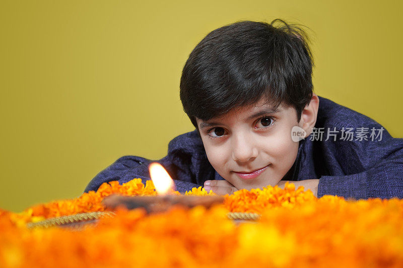 一个快乐微笑的印度亚洲男孩看着一个Pooja或祈祷塔利与火焰，Jyot, Diya, Deepak火焰和金盏花